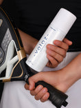 Cargar la imagen en la vista de la galería, Jugadora de pádel sosteniendo un bote de spray antideslizante Velaz TotalGrip junto a su pala.