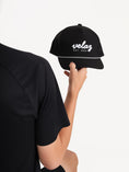 Cargar la imagen en la vista de la galería, Modelo sosteniendo la gorra negra Velaz con detalles blancos para deporte.
